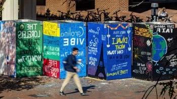 Student walking on brick pathways by murals advertising student groups on the campus of UNC-Chapel Hill.